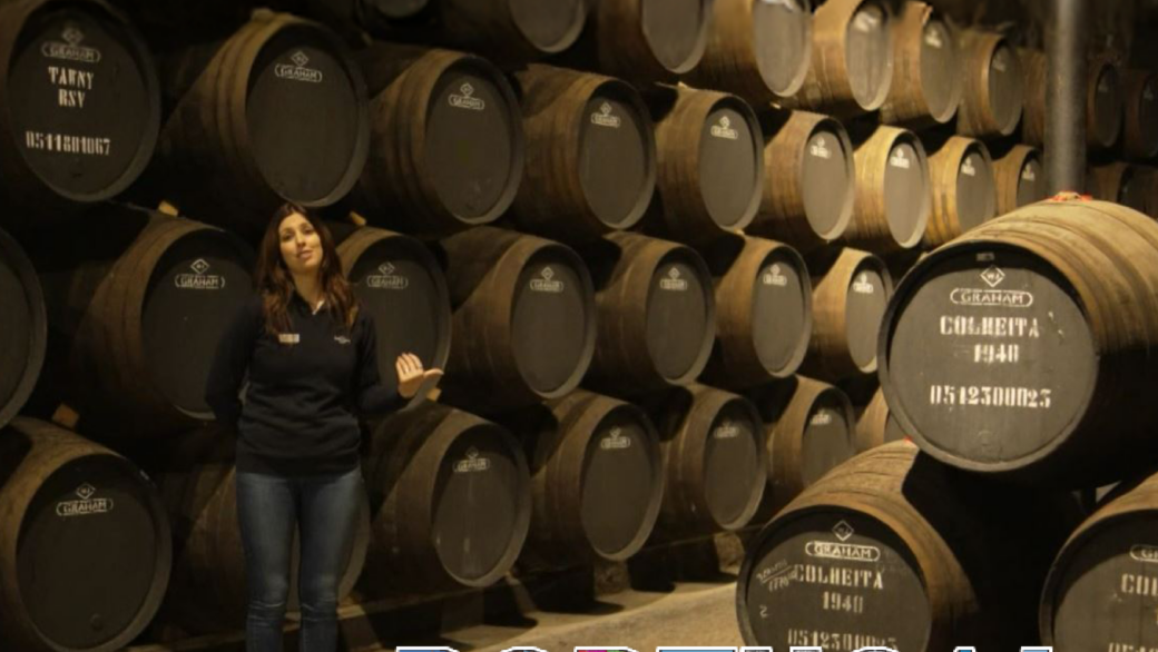 Caves Graham's: Interior das caves históricas com barricas de vinho do Porto a envelhecer, destacando o legado e a tradição das Caves Graham's em Vila Nova de Gaia. Portugal à Vista na CamoesTV.